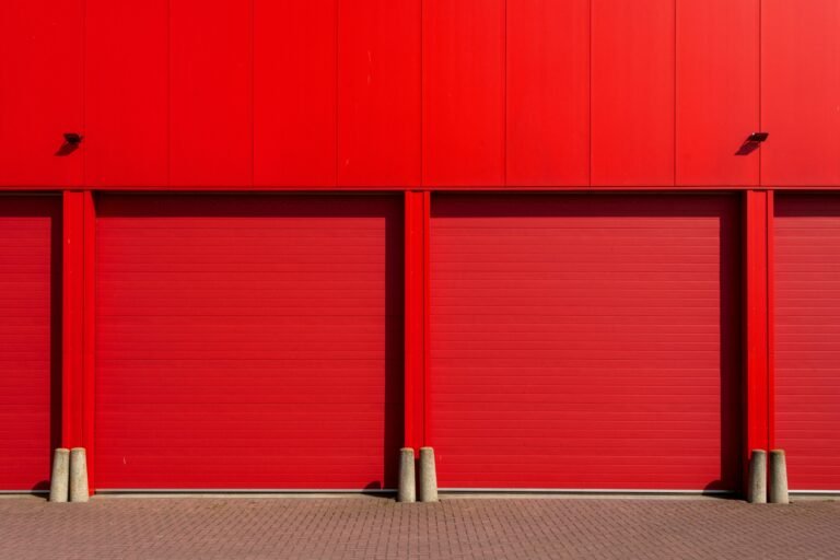 Industrial siding painting project with three red garage doors by Soca Services