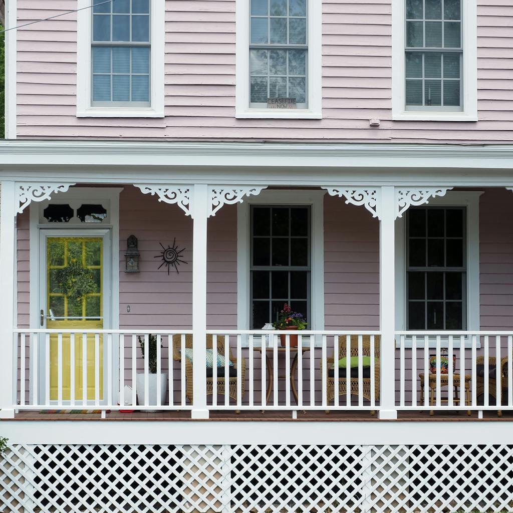 Beautiful pink house with a cozy porch featuring ornate trim, wood siding painted by soca services