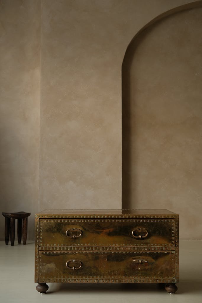 Stylish gold chest in minimalist interior with textured walls and arch detail.