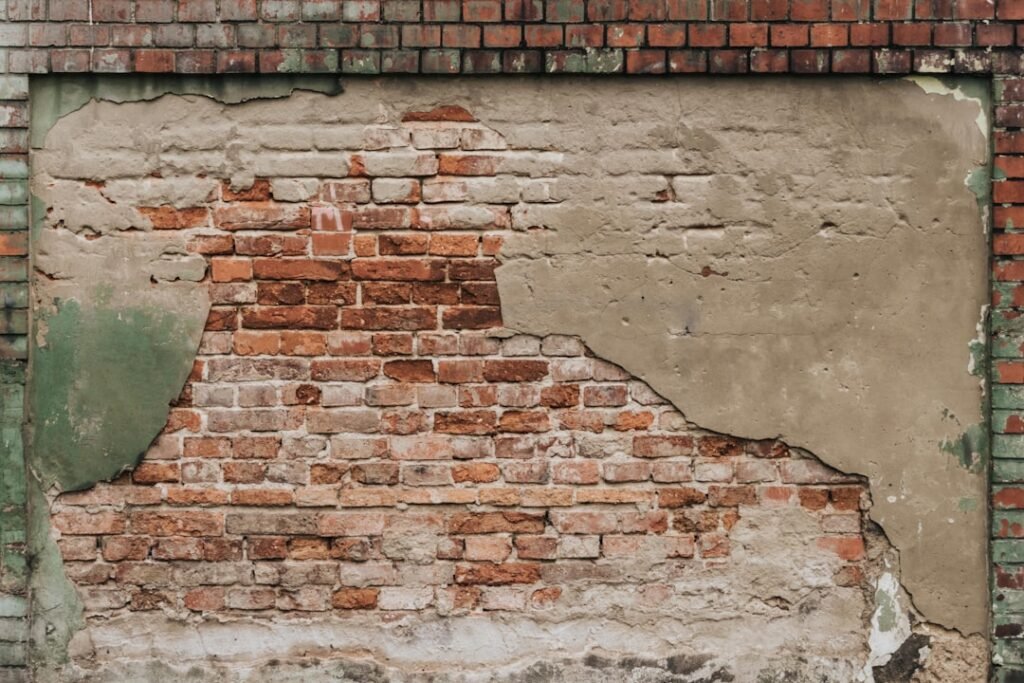 Deteriorated wall showing damaged coating over brick masonry, illustrating moisture and paint failure problems