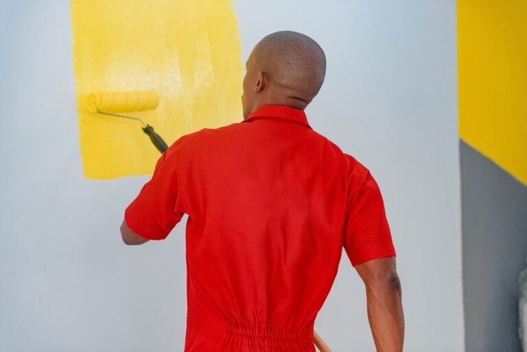 Professional painter in Toronto applying yellow paint to interior wall with roller, demonstrating quality painting services by Mika Baumeister